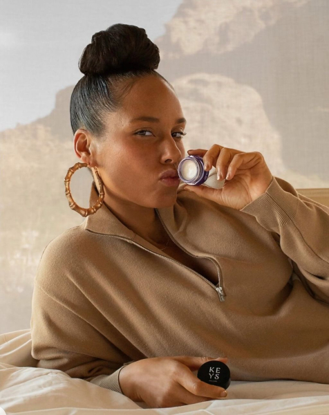 Alicia Keys reclining and kissing a lip balm jar